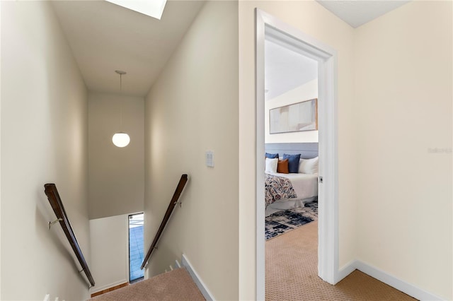 corridor featuring a skylight, baseboards, carpet flooring, and an upstairs landing