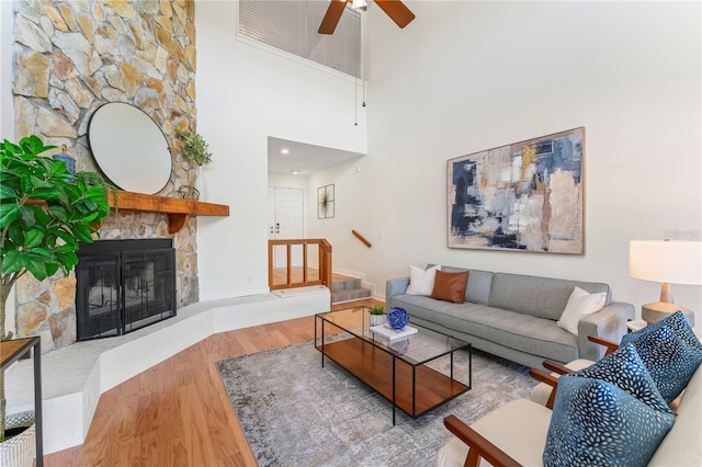 living area with a stone fireplace, a towering ceiling, and wood finished floors