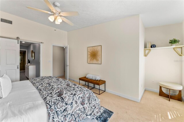 carpeted bedroom with a textured ceiling, a barn door, a ceiling fan, visible vents, and baseboards