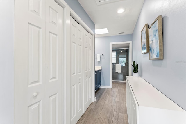 corridor with light wood-type flooring, visible vents, and baseboards