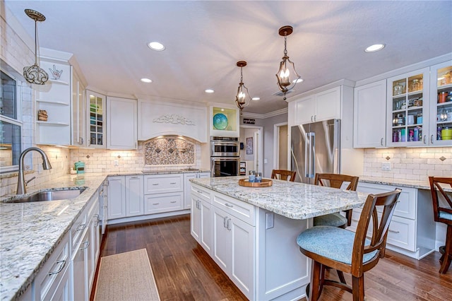 kitchen with appliances with stainless steel finishes, dark wood-type flooring, a kitchen bar, white cabinetry, and a sink