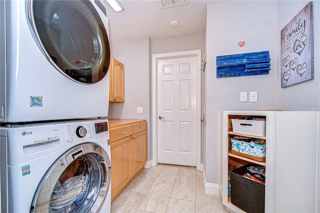 washroom with light tile patterned floors, stacked washer / drying machine, cabinet space, visible vents, and baseboards