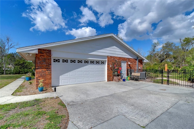 view of side of property with driveway, a garage, fence, central AC, and brick siding