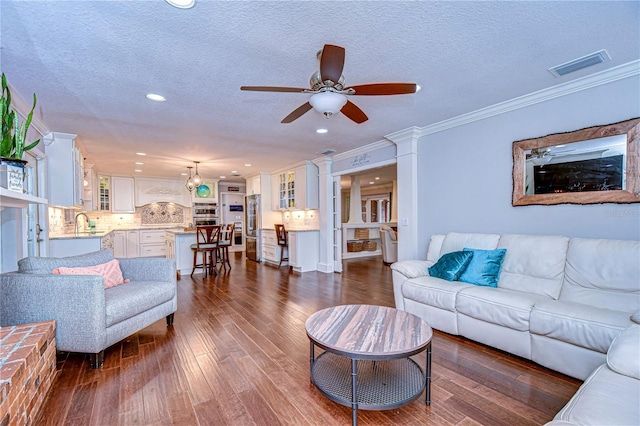 living room featuring ornate columns, crown molding, visible vents, and dark wood-style flooring