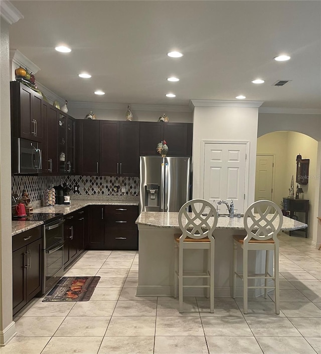 kitchen with tasteful backsplash, appliances with stainless steel finishes, light stone countertops, and a kitchen breakfast bar