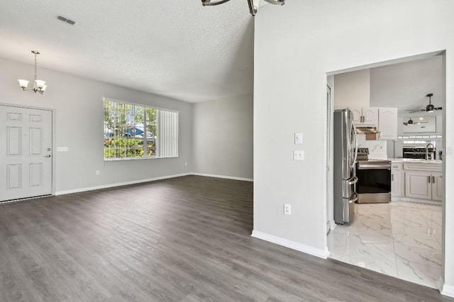 915 Brittany Park Blvd, Tarpon Springs, FL 34689 - unfurnished living room with a chandelier, baseboards, a textured ceiling, a sink, and light wood-style flooring