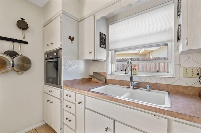 kitchen with tasteful backsplash, light countertops, stainless steel oven, light tile patterned flooring, and a sink