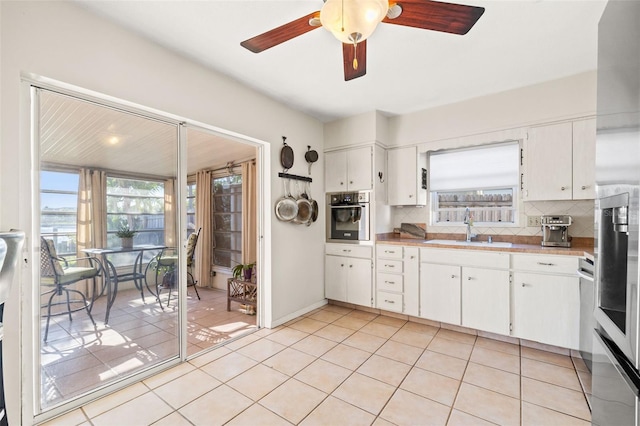 kitchen with a sink, tasteful backsplash, stainless steel oven, a healthy amount of sunlight, and light tile patterned floors