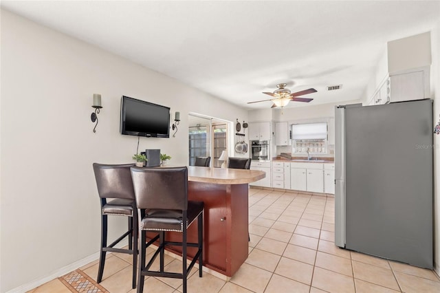 kitchen featuring visible vents, a breakfast bar area, appliances with stainless steel finishes, a peninsula, and white cabinetry