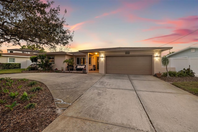 view of front facade with stucco siding, an attached garage, concrete driveway, and fence