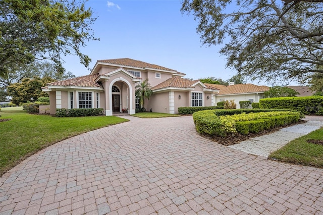 mediterranean / spanish home with a tiled roof, a front yard, decorative driveway, and stucco siding