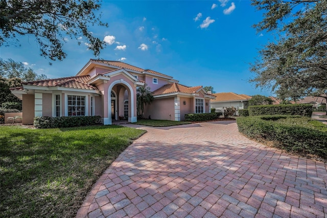 mediterranean / spanish house featuring a front yard, decorative driveway, a tiled roof, and stucco siding