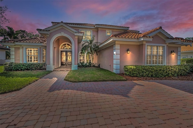 mediterranean / spanish home featuring french doors, a lawn, a tiled roof, and stucco siding