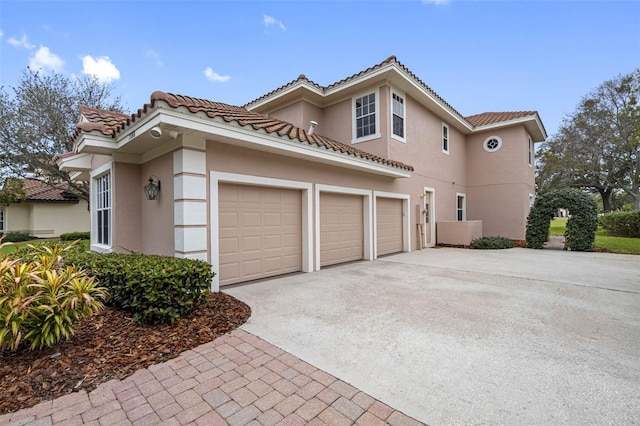 view of side of property with a garage, a tile roof, concrete driveway, and stucco siding