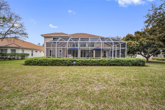 back of property with glass enclosure, a tile roof, and a lawn