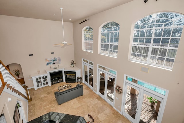 living area with a high ceiling, a glass covered fireplace, a ceiling fan, and baseboards