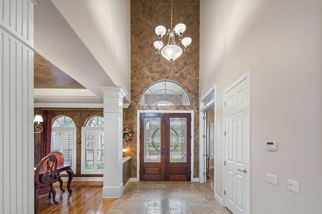 foyer entrance featuring french doors, crown molding, a high ceiling, and an inviting chandelier