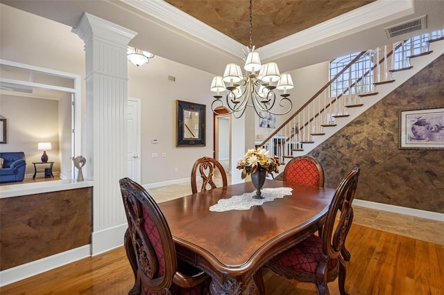 dining space featuring wood finished floors, visible vents, stairs, a tray ceiling, and decorative columns