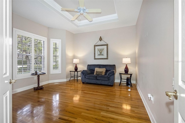 living area with ornamental molding, wood finished floors, a raised ceiling, and baseboards