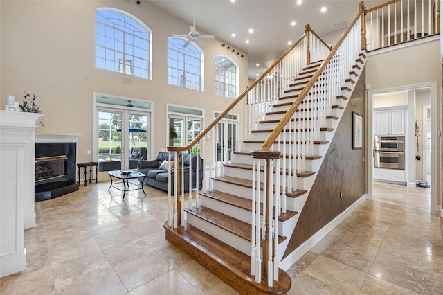 stairs featuring visible vents, baseboards, a towering ceiling, ceiling fan, and a fireplace