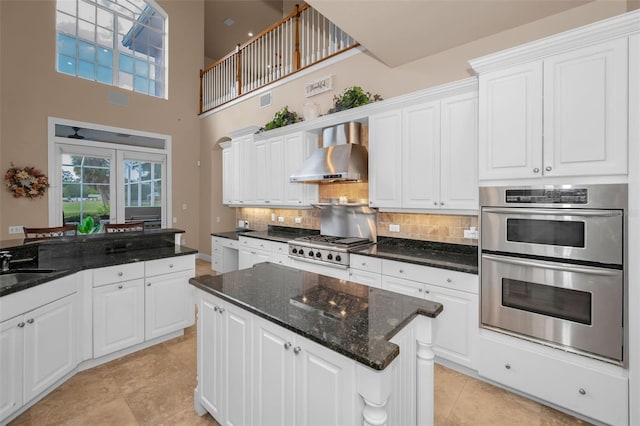 kitchen with appliances with stainless steel finishes, white cabinets, backsplash, and wall chimney exhaust hood