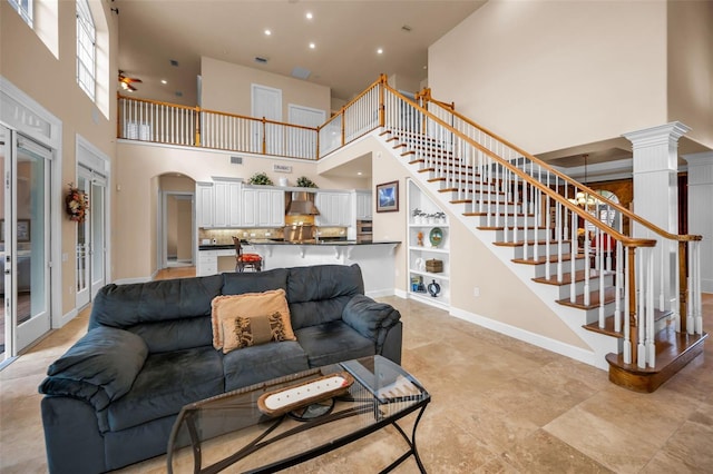 living room featuring baseboards, arched walkways, a towering ceiling, stairway, and ornate columns