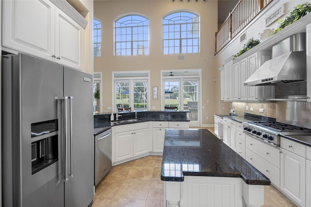 kitchen featuring a peninsula, a sink, white cabinets, appliances with stainless steel finishes, and wall chimney exhaust hood