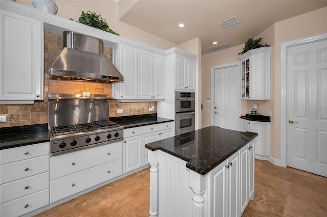 kitchen featuring stainless steel appliances, white cabinetry, wall chimney range hood, decorative backsplash, and glass insert cabinets