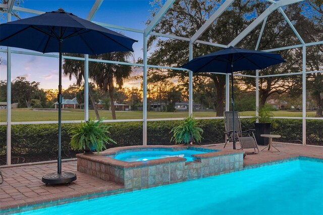 pool at dusk featuring a lawn, a patio area, an in ground hot tub, a lanai, and an outdoor pool