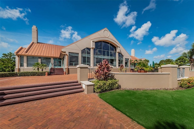 back of house featuring a fenced front yard, a chimney, stucco siding, a standing seam roof, and metal roof