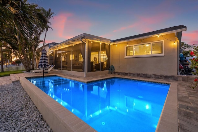 pool at dusk with an outdoor pool, fence, and a sunroom