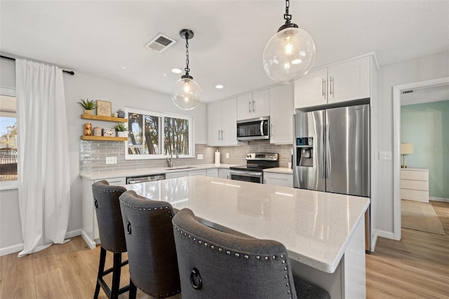 kitchen featuring visible vents, light wood finished floors, decorative backsplash, appliances with stainless steel finishes, and a kitchen breakfast bar