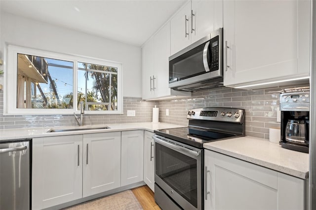 kitchen with tasteful backsplash, white cabinets, appliances with stainless steel finishes, and a sink