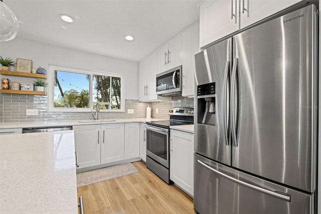 kitchen featuring a sink, tasteful backsplash, white cabinetry, light wood-style floors, and appliances with stainless steel finishes