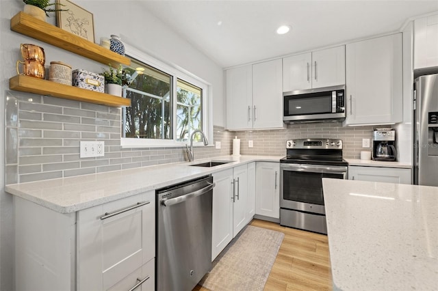 kitchen featuring backsplash, stainless steel appliances, light wood-style floors, white cabinetry, and a sink