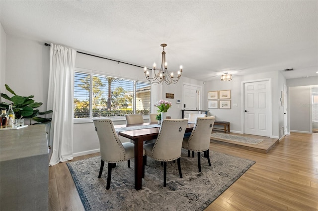 dining room with baseboards, visible vents, an inviting chandelier, a textured ceiling, and light wood-type flooring