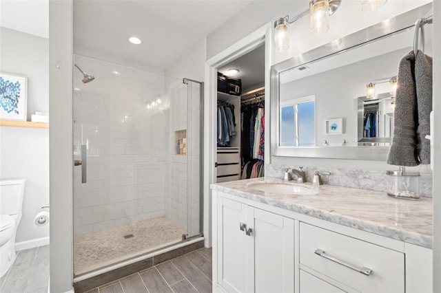 bathroom with a spacious closet, wood finish floors, toilet, a stall shower, and vanity