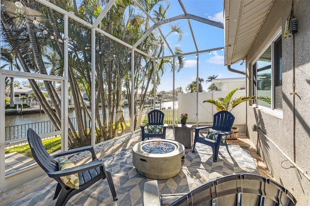 view of patio featuring glass enclosure, a water view, a fire pit, and fence