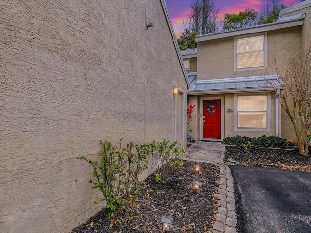 exterior entry at dusk featuring a standing seam roof, metal roof, and stucco siding