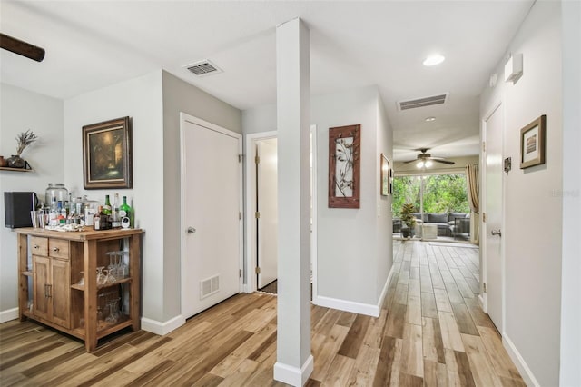 hall with light wood-type flooring, visible vents, and baseboards