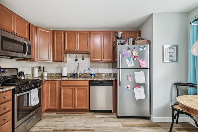 kitchen featuring stainless steel appliances, a sink, tasteful backsplash, brown cabinetry, and dark stone countertops