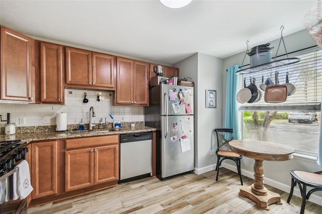 kitchen with stainless steel appliances, brown cabinetry, a sink, and tasteful backsplash