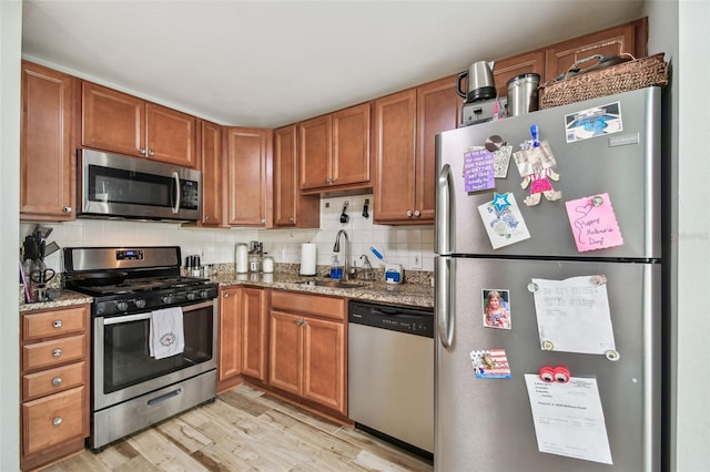 kitchen with stainless steel appliances, a sink, decorative backsplash, and dark stone countertops