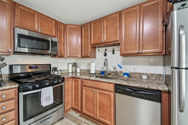 kitchen featuring light stone countertops, stainless steel appliances, a sink, brown cabinets, and decorative backsplash