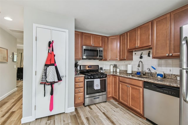 kitchen featuring a sink, appliances with stainless steel finishes, light wood finished floors, dark stone countertops, and tasteful backsplash