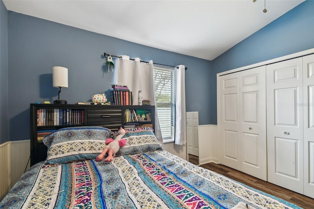 bedroom with dark wood finished floors, a closet, wainscoting, and vaulted ceiling