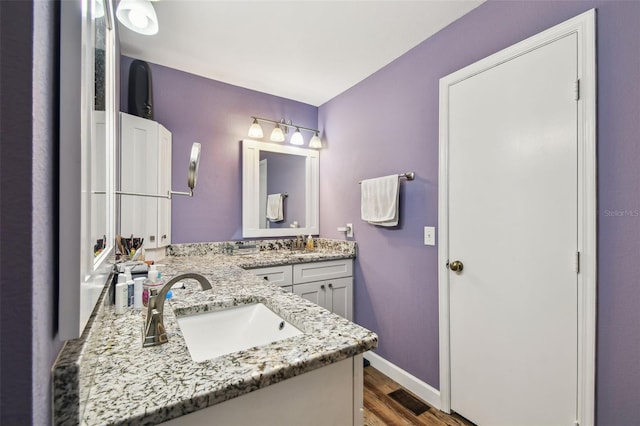 bathroom with double vanity, visible vents, baseboards, wood finished floors, and a sink