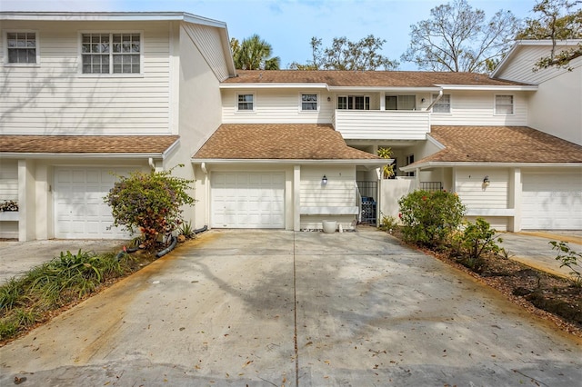 multi unit property featuring concrete driveway, roof with shingles, an attached garage, and stucco siding