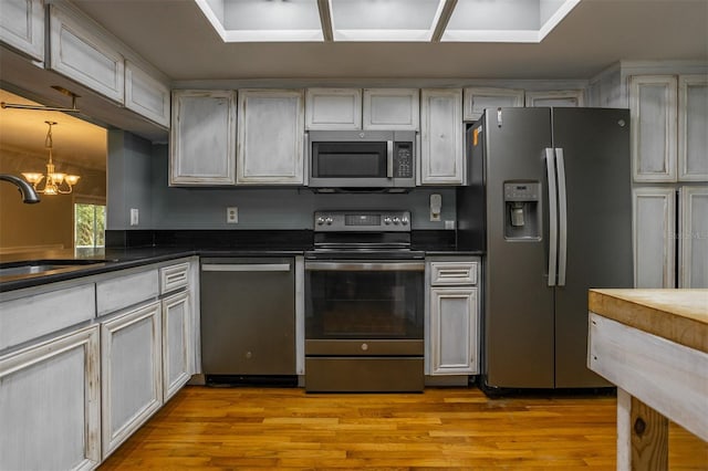 kitchen featuring dark countertops, appliances with stainless steel finishes, a sink, light wood-style floors, and a notable chandelier