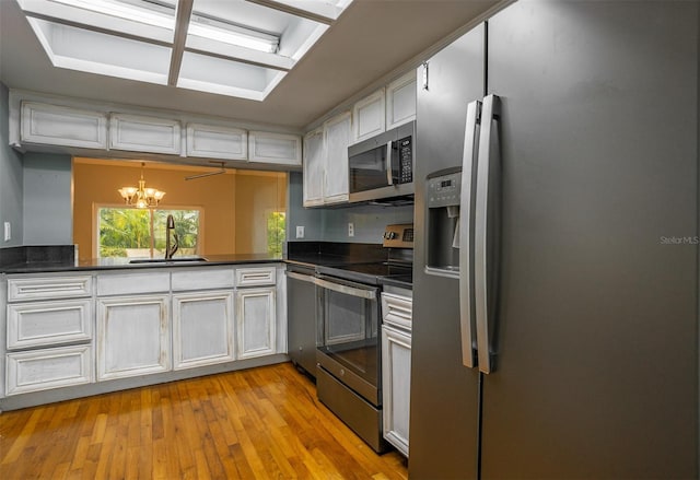 kitchen with white cabinets, dark countertops, decorative light fixtures, stainless steel appliances, and a sink